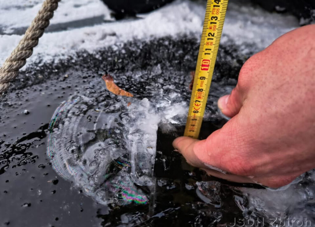 Ruka s metrem měří tloušťku ledu